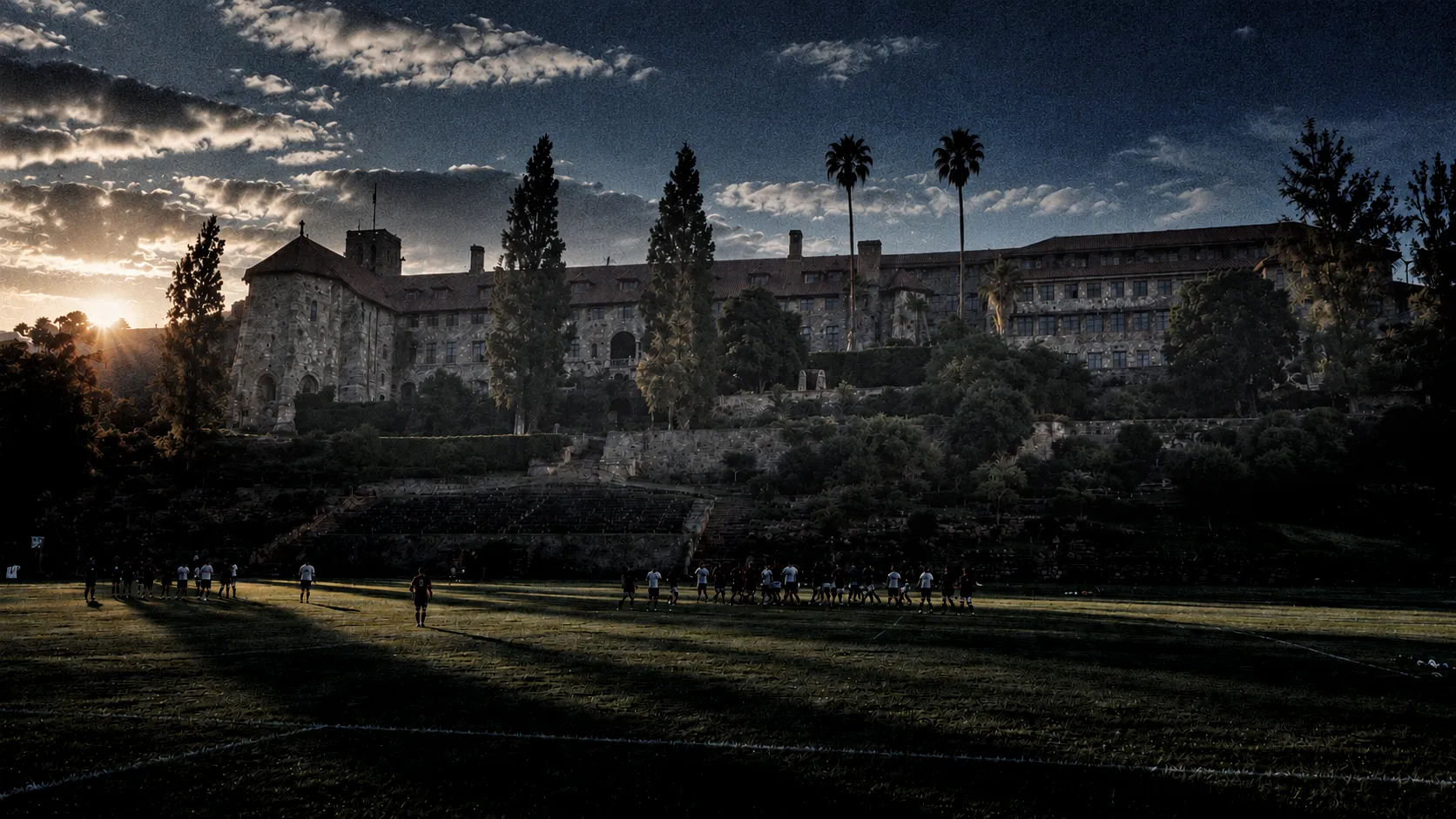 School rugby on a grass field at sunset, in front of a historic stone building.